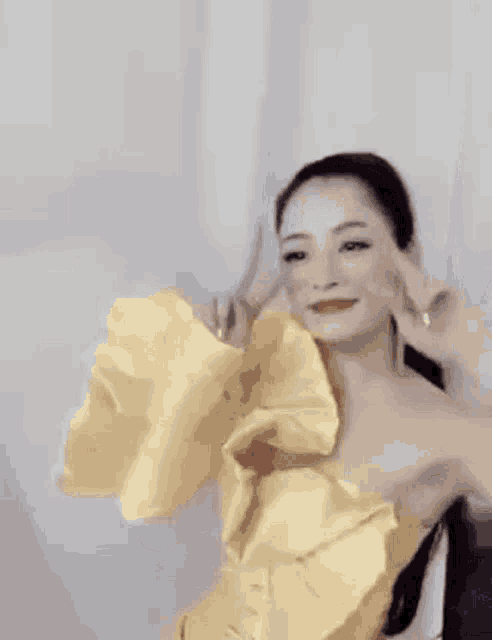 a woman in a yellow dress with a large flower on her shoulder is making a peace sign .