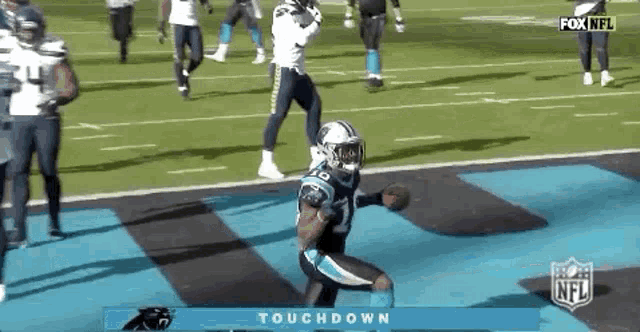 a football player in a carolina panthers uniform is jumping in the air while holding a football .