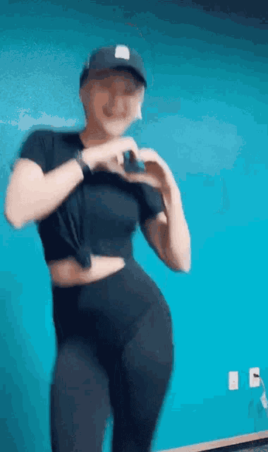 a woman is making a heart shape with her hands while wearing a hat .