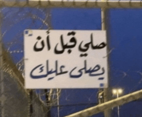 a sign with arabic writing on it hangs from a fence