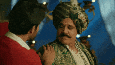 a man in a turban with a red circle on his forehead talks to another man