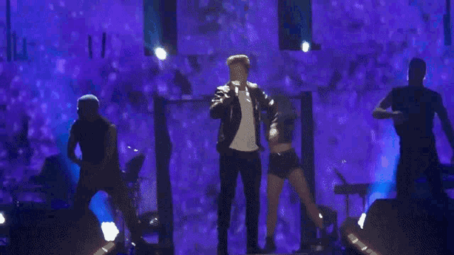 a man in a white shirt is dancing on a stage in front of purple lights