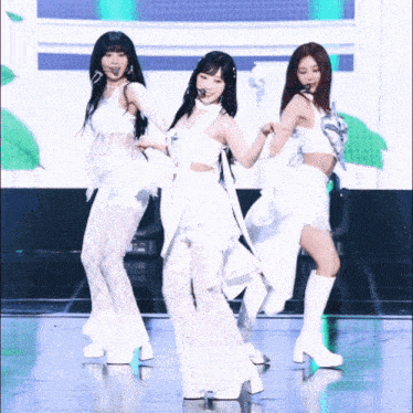 three women are dancing on a stage wearing white dresses