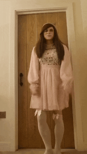 a woman in a pink dress is standing in front of a door