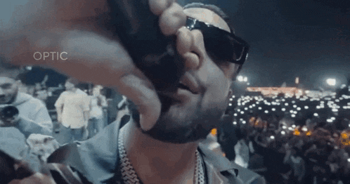 a man wearing sunglasses is singing into a microphone in front of a crowd with the word optic on the bottom