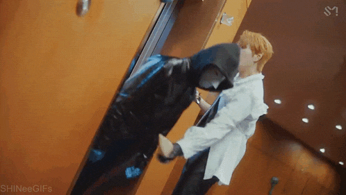 two men are standing next to each other in an elevator . one of the men is wearing a hooded jacket .