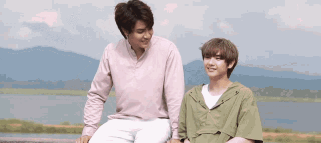 two young men are standing next to each other in front of a body of water