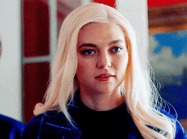 a woman with blonde hair and blue eyes is wearing a blue jacket and black top .