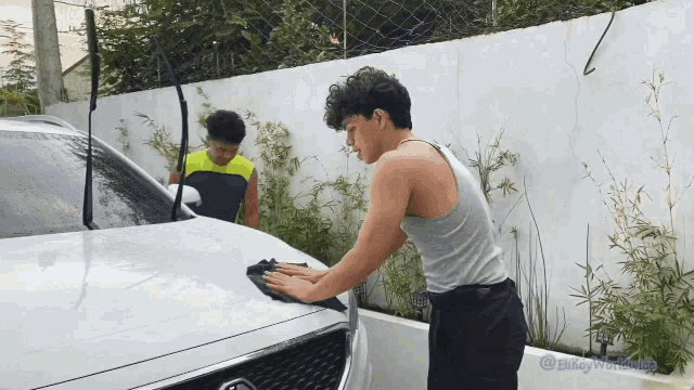 a man in a tank top is cleaning a car