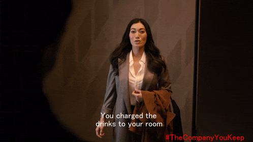 a woman in a suit is standing in a dark room and says you charged the drinks to your room