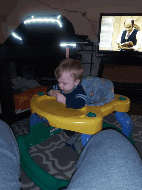 a baby sits in a yellow and green walker in front of a television