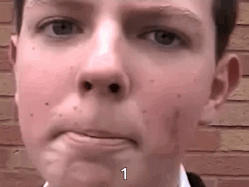 a close up of a boy 's face with a brick wall in the background and the number 1 on his face .