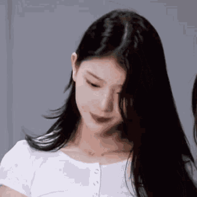 a woman with long black hair and a white shirt is looking down .