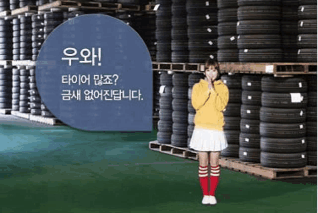 a woman in a yellow hoodie is standing in front of a pile of tires .