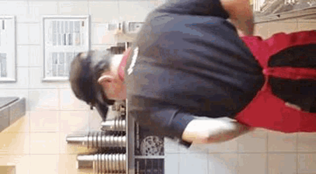 a man in a black shirt and red apron is standing in front of a counter .