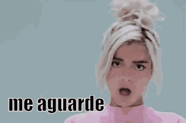 a woman in a pink sweater is making a funny face and saying `` me aguarde '' .