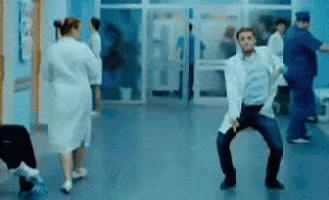 a man in a lab coat is dancing in a hospital corridor