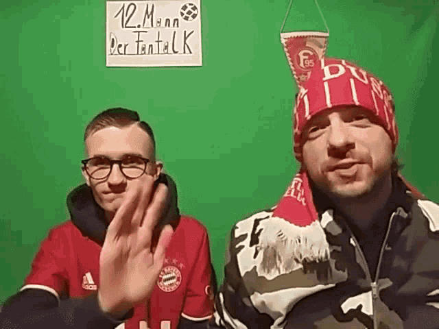 two men standing in front of a green wall with a sign that says 12 mann per fantack