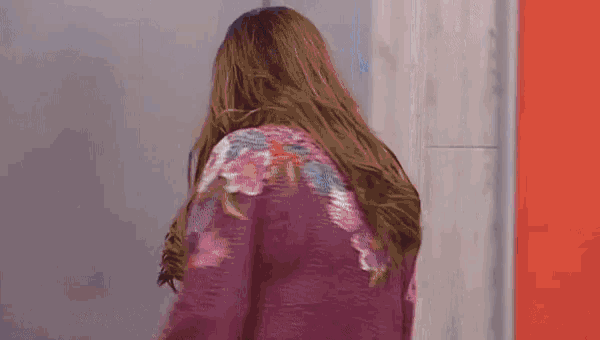 a woman in a purple jacket with flowers on the back is standing in front of a red wall .