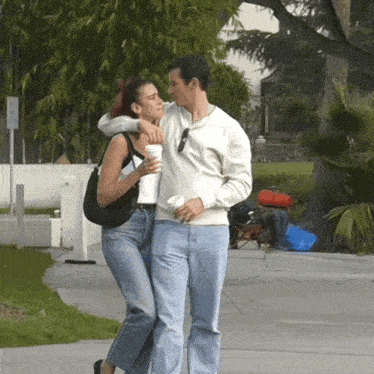 a man and a woman are walking down a sidewalk and the man is holding a cup of coffee