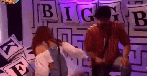 a man and a woman are standing in front of a wall that has the word big on it