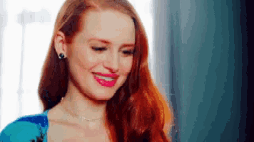 a woman with long red hair is smiling and wearing a blue shirt .