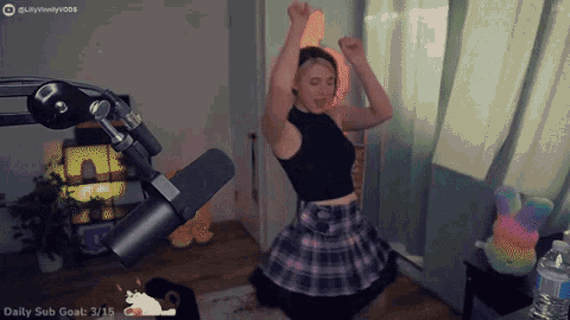 a woman in a plaid skirt is dancing in front of a microphone with the words daily sub goat 3/15 on the bottom right