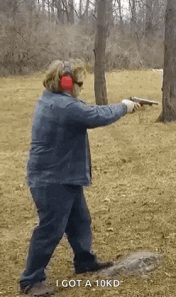 a woman is holding a gun in a field while wearing headphones .