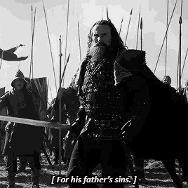 a black and white photo of a man with a beard holding a sword and saying for his father 's sins