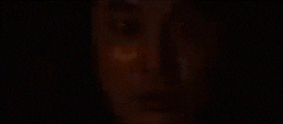 a close up of a man 's face in a dark room with a woman behind him .