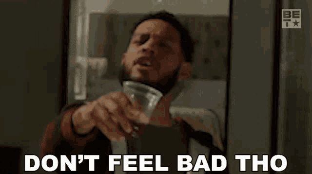 a man with a beard is holding a glass of water and saying `` do n't feel bad tho '' .