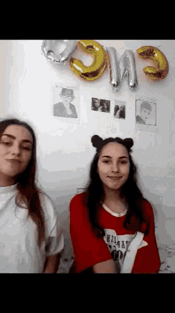 two girls are standing in front of a wall with balloons that spell out the word om3
