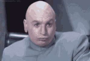 a bald man in a suit is making a funny face while sitting in a chair .