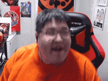 a man wearing glasses and an orange shirt sitting in a cer chair