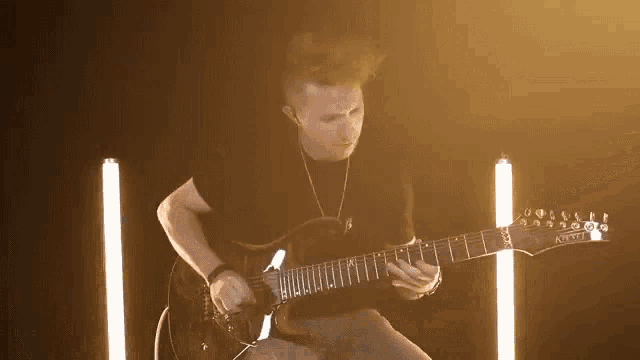 a man in a black shirt is playing an electric guitar in a dark room with lights behind him .