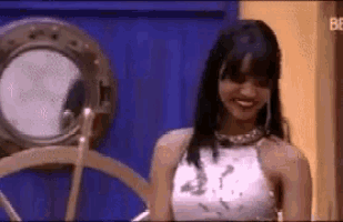 a woman in a white top is smiling in front of a ship wheel .