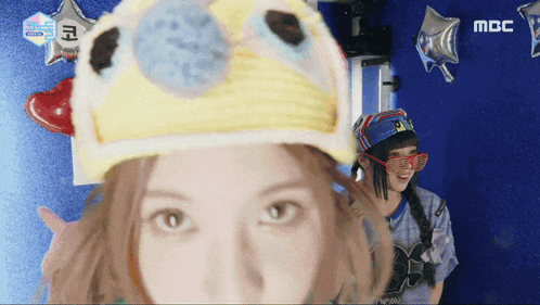 a woman wearing a hat and sunglasses is standing next to another woman wearing a mbc shirt