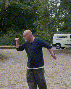 a bald man in a blue shirt is dancing in a parking lot with a white van in the background that says ' enterprise '