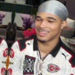a man wearing a gray headband and a white shirt with the letter s on it is smiling
