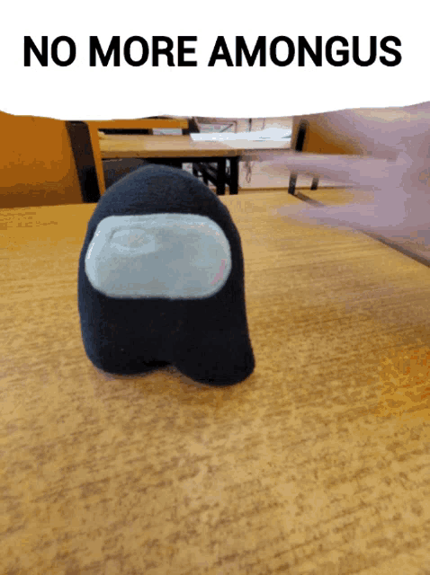 a black among us stuffed animal is sitting on a wooden table under a sign that says no more amongus