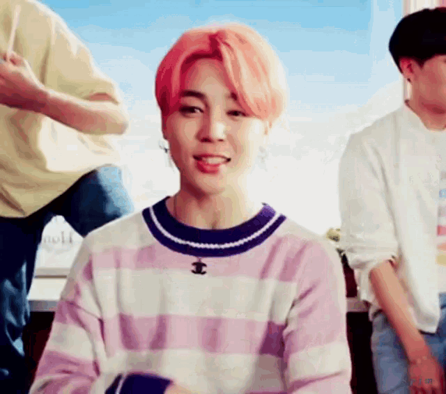 a young man with pink hair is wearing a striped sweater and a necklace with the letter t on it