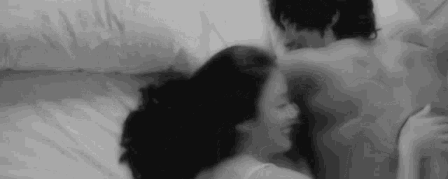 a black and white photo of a man and a woman laying in bed .