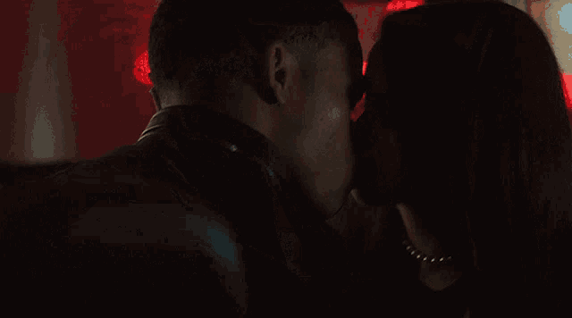 a man and woman kissing in a dark room with red lights behind them