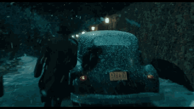 a black car is driving down a snowy street in front of a building