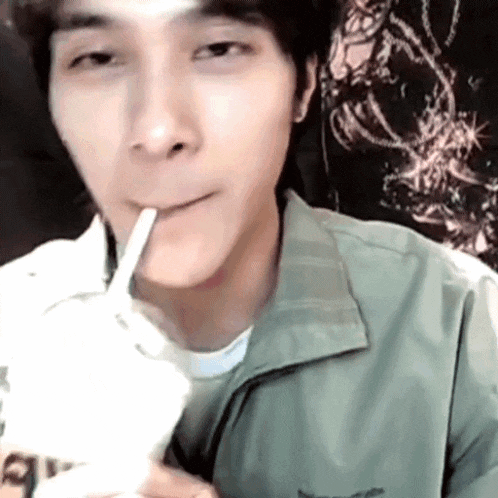 a man in a green jacket is drinking from a plastic straw .