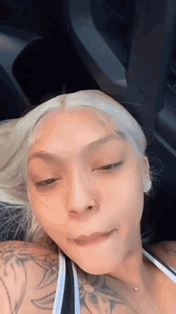 a woman with blonde hair and tattoos is sitting in a car with her eyes closed .