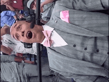 a man wearing a suit and a pink bow tie is talking into a microphone