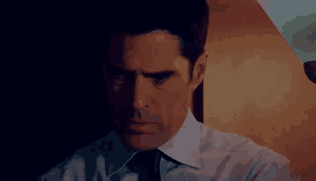 a man in a white shirt and tie is looking down at something in the dark .