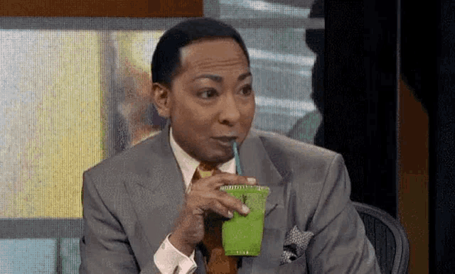 a man in a suit and tie is drinking a green juice through a straw .