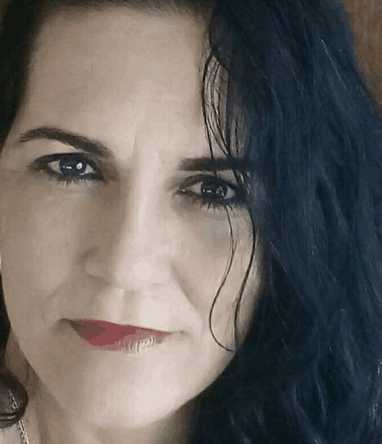 a woman with blue hair and red lips looks at the camera